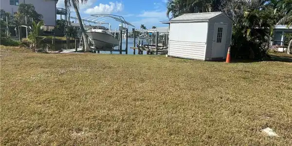 Image 4: View of green lawn featuring boat lift, a dock, a water view, and an outbuilding