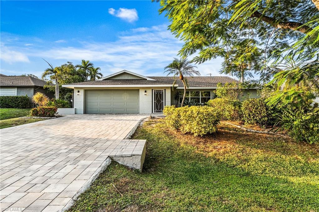 Image 2: Ranch-style home with decorative driveway, stucco siding, a garage, and a front lawn with a beautiful Royal Ponciana tree in front yard.