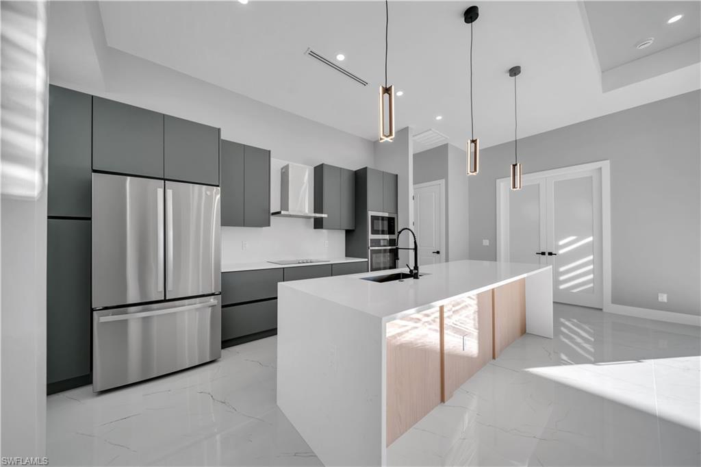 Image 4: Kitchen featuring stainless steel appliances, light marble finish floors, an island with sink, decorative light fixtures, and recessed lighting