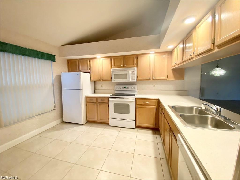 Image 2: Kitchen featuring white appliances, lofted ceiling, light countertops, light tile patterned flooring, and light wood finish cabinets