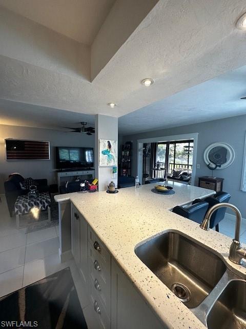 Image 2: Kitchen with light stone counters, open floor plan, light tile patterned flooring, a ceiling fan, and a textured ceiling