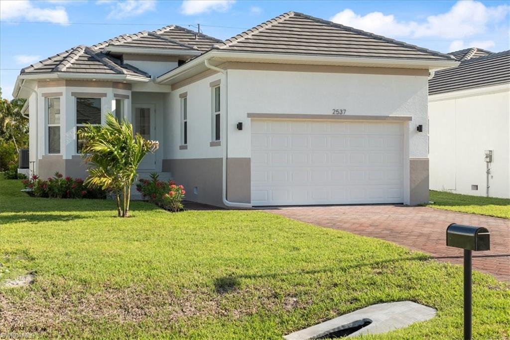 Image 1: Ranch-style home with a tile roof, a front yard, decorative driveway, an attached garage, and stucco siding