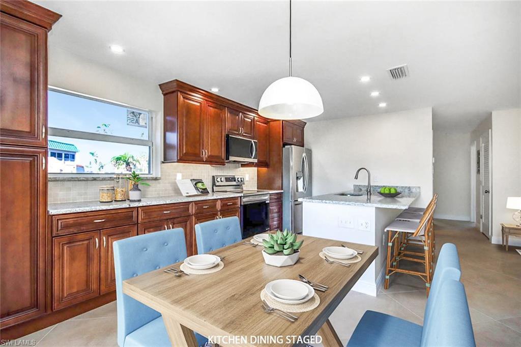 Image 3: Kitchen featuring light tile patterned floors, stainless steel appliances, tasteful backsplash, hanging light fixtures, and a breakfast bar