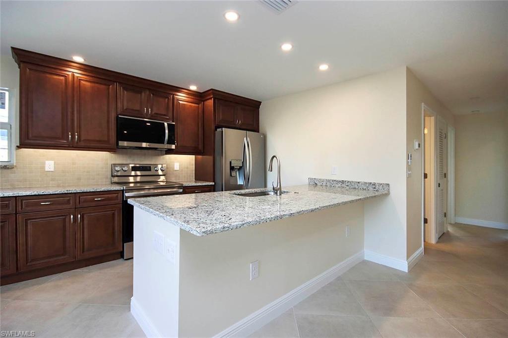 Image 4: Kitchen with appliances with stainless steel finishes, sink, kitchen peninsula, light stone counters, and light tile patterned floors