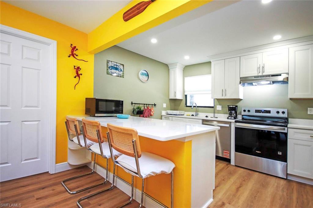 Image 3: Kitchen with white cabinets, a breakfast bar, appliances with stainless steel finishes,