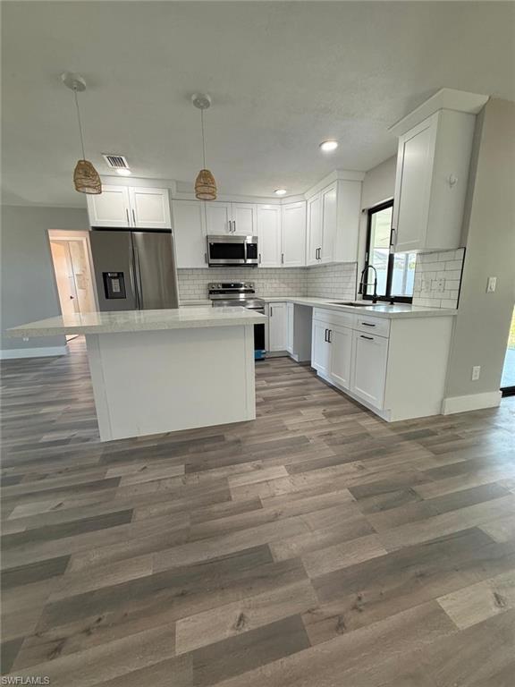 Image 2: Kitchen featuring wood finished floors, a sink, white cabinets, backsplash, and appliances with stainless steel finishes