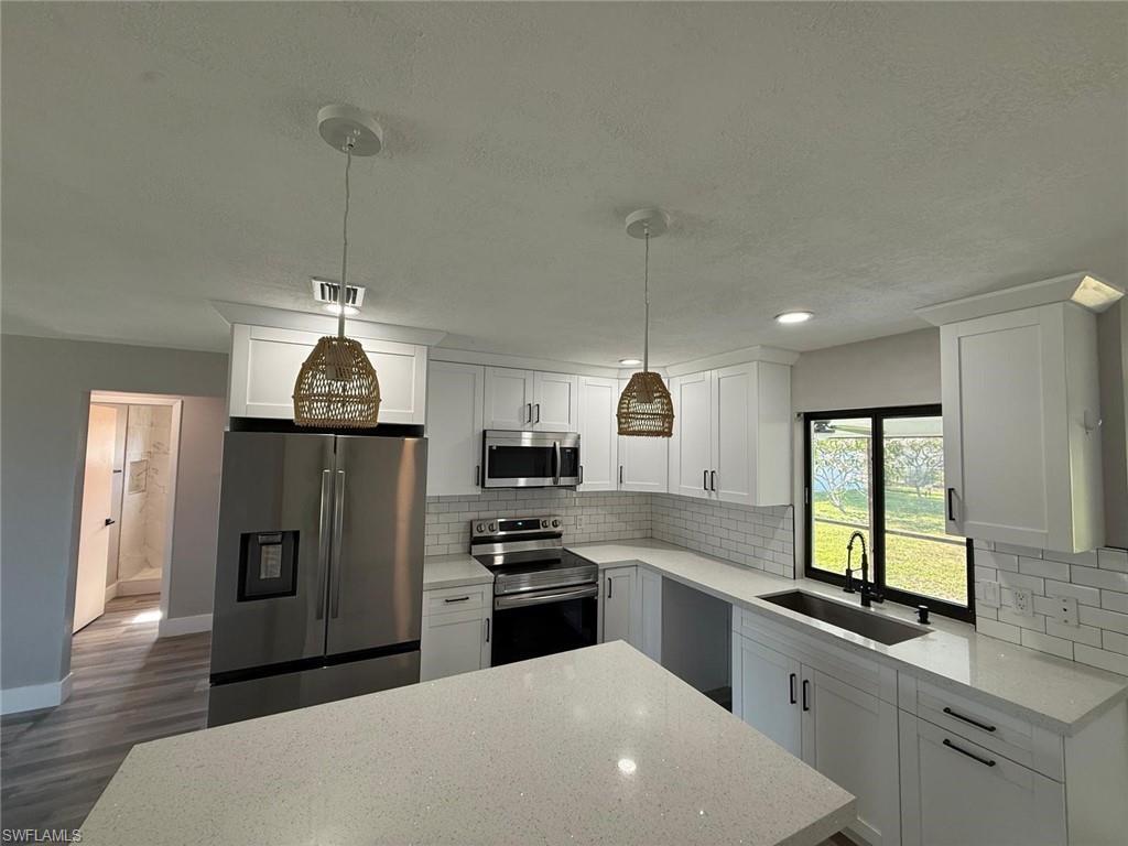 Image 3: Kitchen with a textured ceiling, a sink, decorative backsplash, appliances with stainless steel finishes, and dark wood-style floors