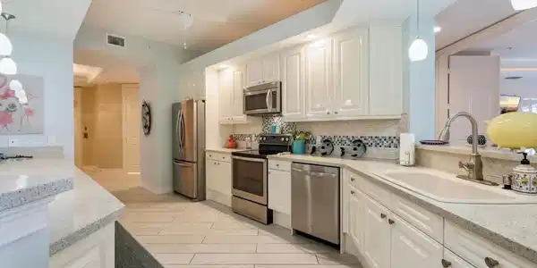 Image 4: Kitchen with decorative light fixtures, light stone counters, stainless steel appliances, and decorative backsplash