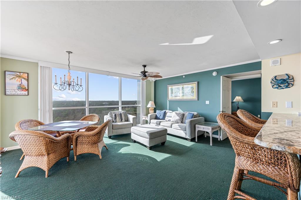 Image 3: Carpeted living room featuring crown molding, ceiling fan with notable  Virtually edited imagechandelier, and expansive windows