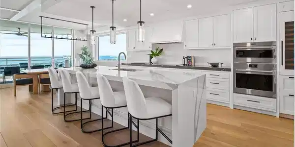 Image 4: The chef's kitchen features Wolf and Sub-Zero appliances, quartz countertops, oversized island, wine cooler, refrigerator and freezer drawers, with water views just beyond