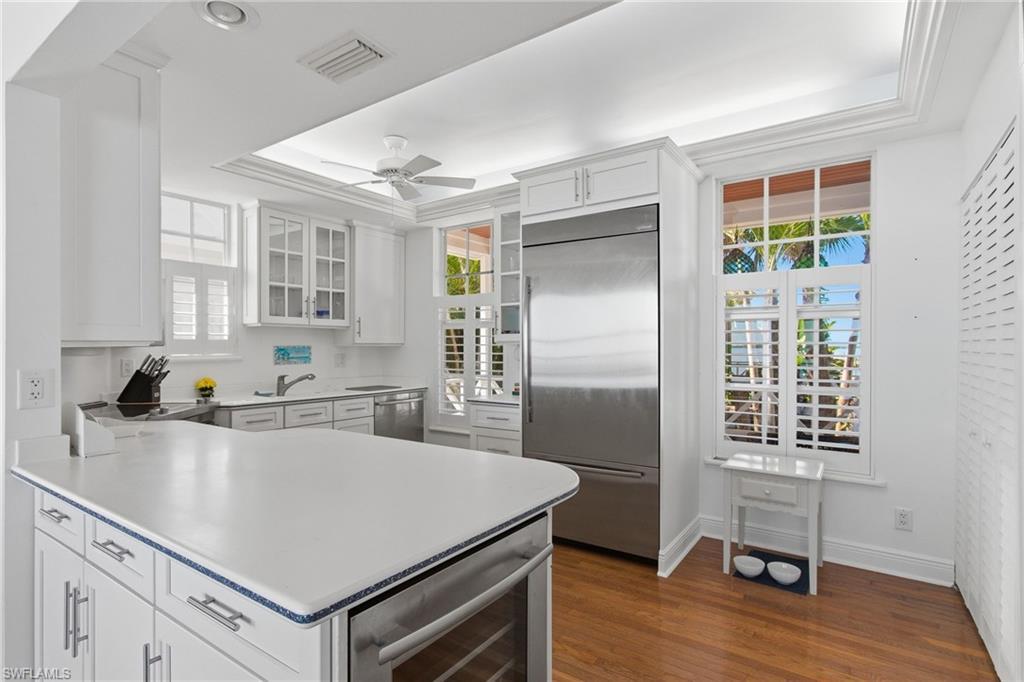 Image 4: Kitchen with appliances with stainless steel finishes, a raised ceiling, a peninsula, light countertops, and glass insert cabinets
