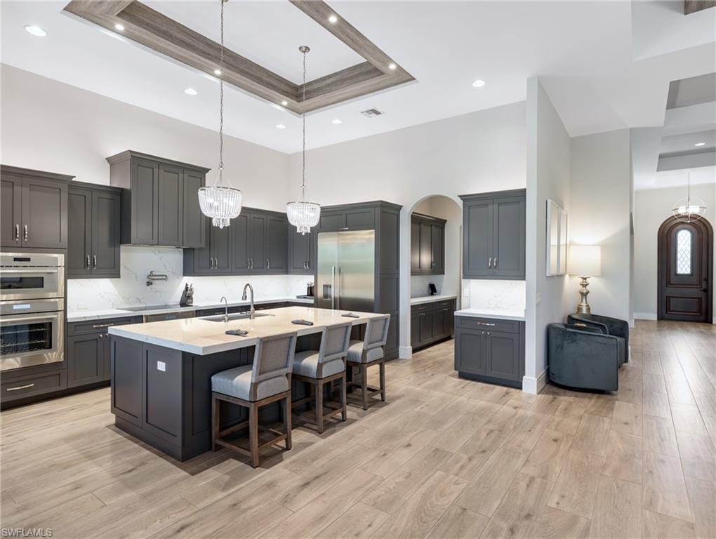 Image 3: Kitchen featuring a kitchen bar, decorative backsplash, pendant lighting, a tray ceiling, and a high ceiling