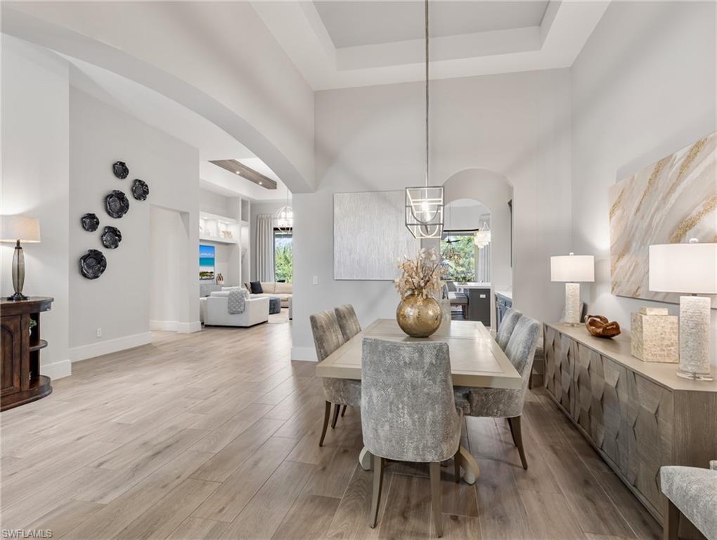Image 4: Dining room featuring arched walkways, a raised ceiling, plenty of natural light, light wood-type flooring, and a towering ceiling
