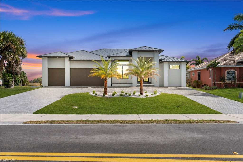 Image 1: Modern home featuring a standing seam roof, a metal roof, a front yard, decorative driveway, and a garage