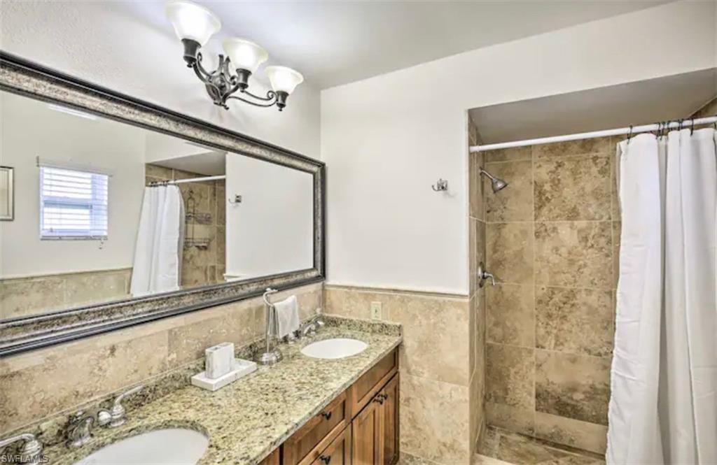 Image 4: Bathroom featuring double vanity, a shower stall, a wainscoted wall, tile walls, and hanging lights