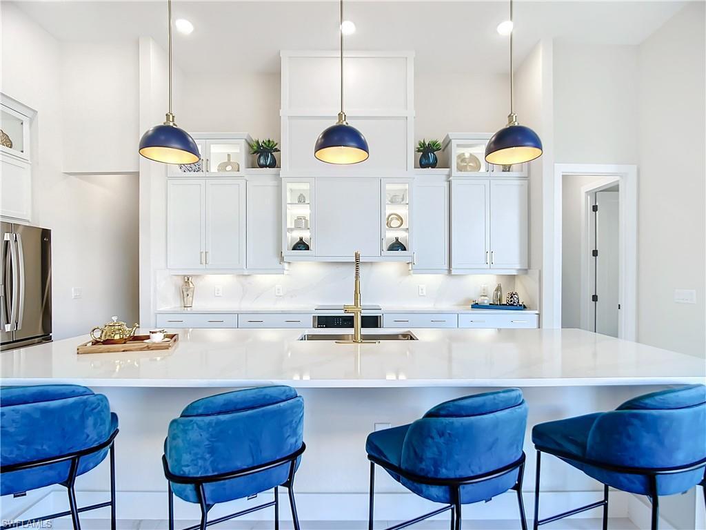 Image 3: Kitchen featuring hanging light fixtures, stainless steel fridge, and white cabinets