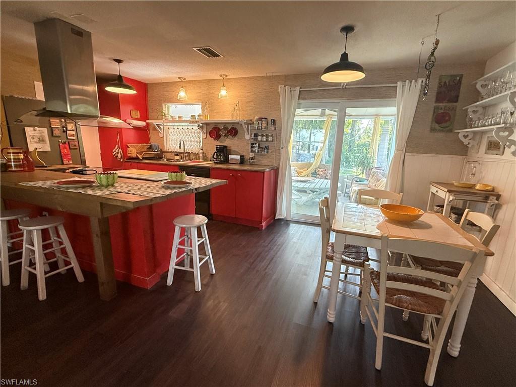 Image 4: Kitchen featuring island exhaust hood, dark wood-style floors, wainscoting, a kitchen breakfast bar, and a sink