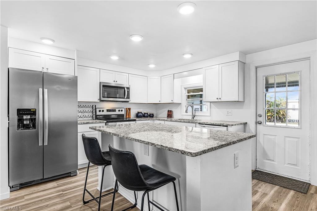 Image 1: Kitchen featuring stainless steel appliances, light stone countertops, white cabinetry, a breakfast bar area, and a center island