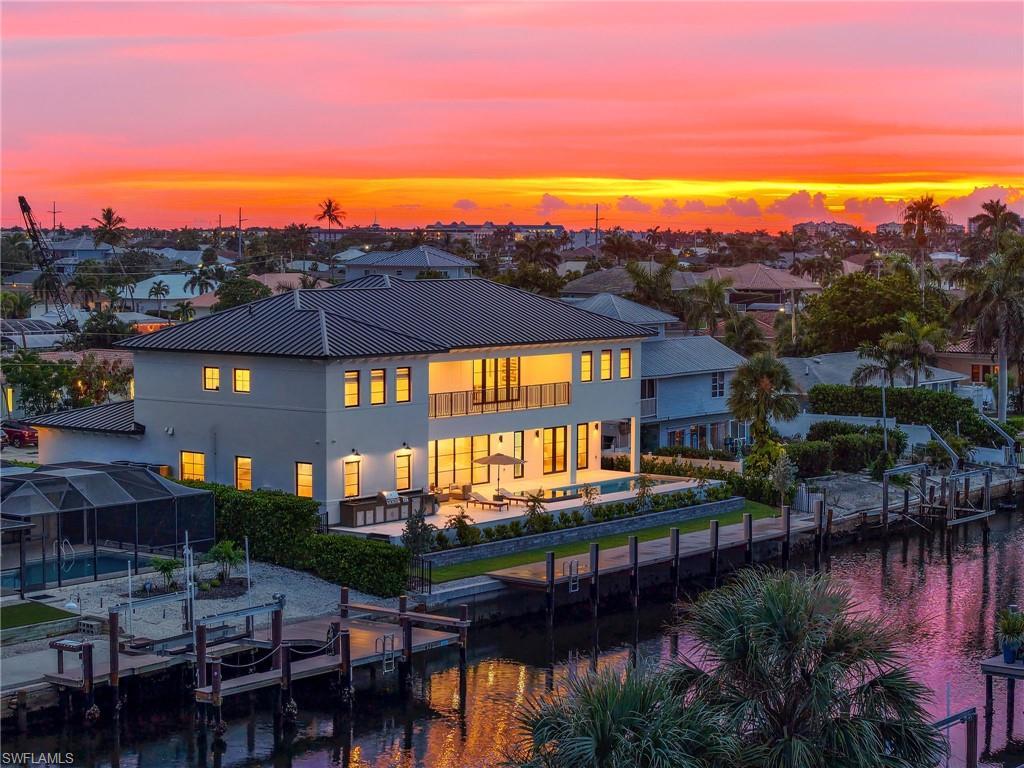 Image 3: Back of property at dusk featuring an outdoor pool, a patio, stucco siding, a balcony, and a metal roof