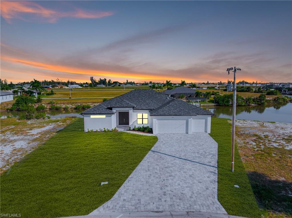 Image 2: View of front of property featuring an attached garage, a lawn, decorative driveway, and stucco siding