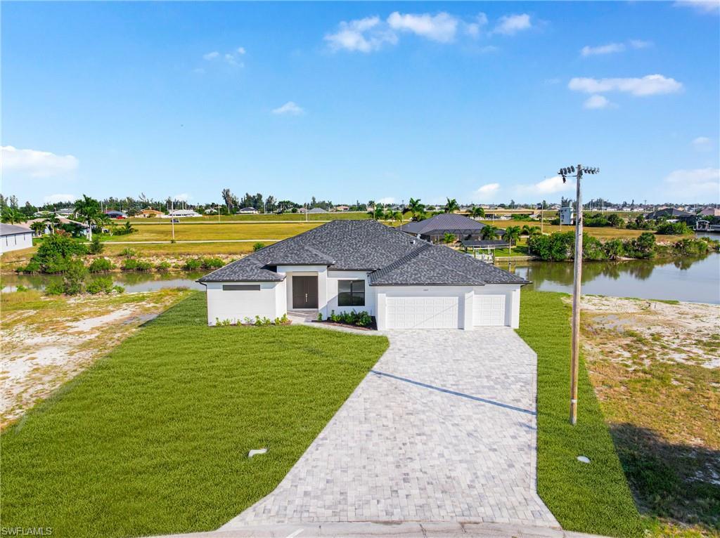 Image 4: View of front of home featuring a garage, decorative driveway, a front lawn, and a water view
