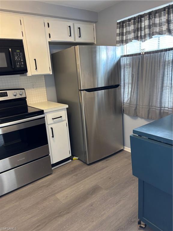 Image 3: Kitchen featuring range, stainless steel fridge, white cabinets, light countertops, and wood finished floors