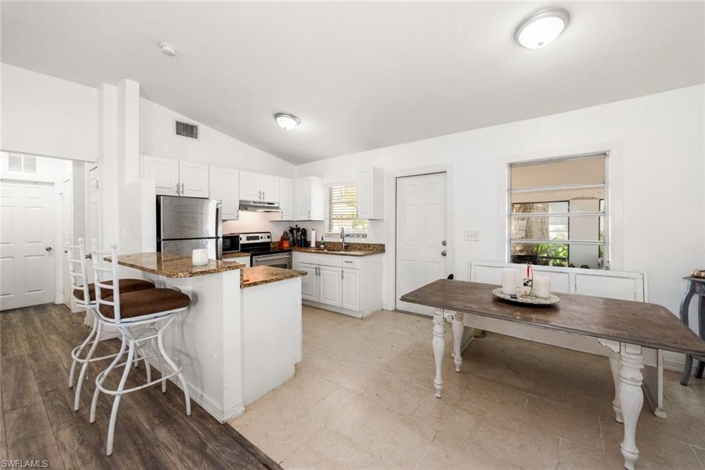 Image 2: Kitchen featuring a breakfast bar area, stainless steel appliances, white cabinets, vaulted ceiling, and dark stone countertops