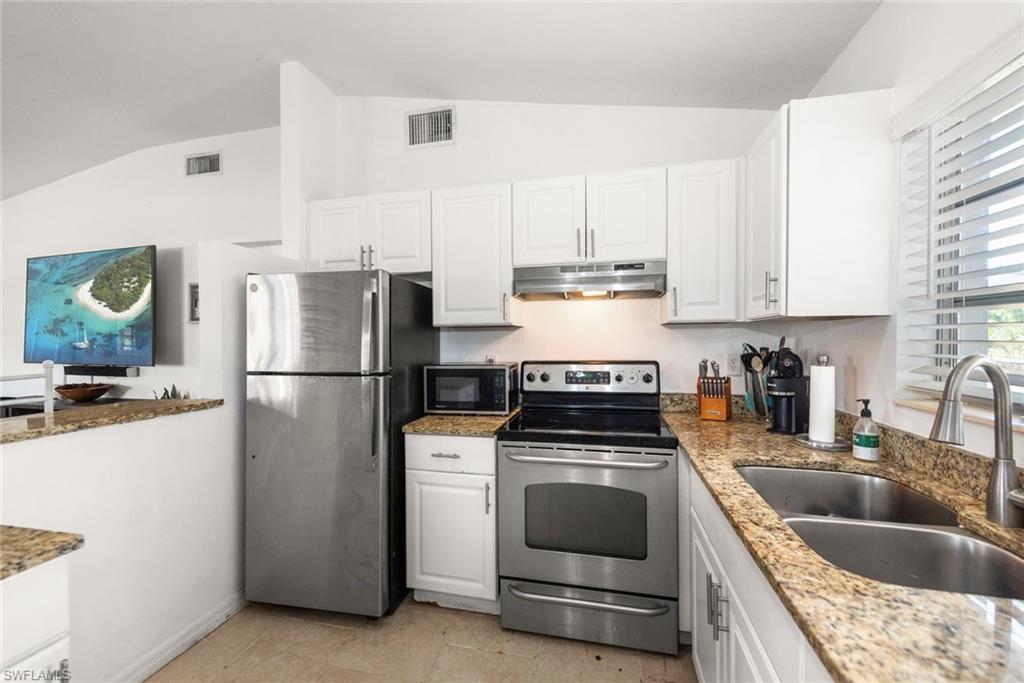 Image 3: Kitchen featuring stainless steel appliances, lofted ceiling, white cabinetry, and light stone counters