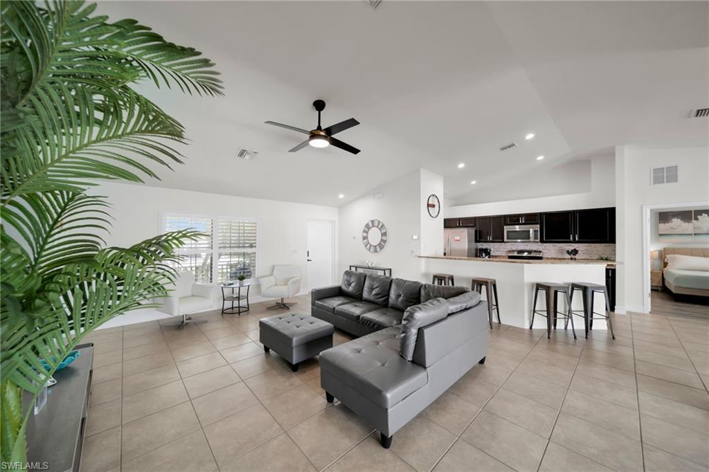 Image 4: Living area with light tile patterned floors, visible vents, a ceiling fan, and vaulted ceiling
