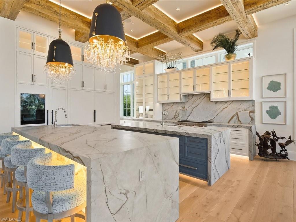Image 4: Kitchen with a breakfast bar area, light stone countertops, light wood-style floors, hanging light fixtures, and white cabinets