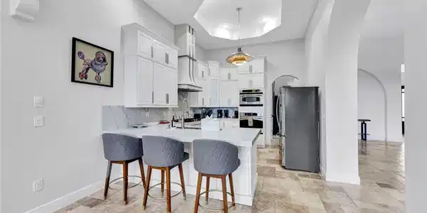 Image 4: Kitchen featuring arched walkways, a breakfast bar, decorative backsplash, a peninsula, and white cabinets
