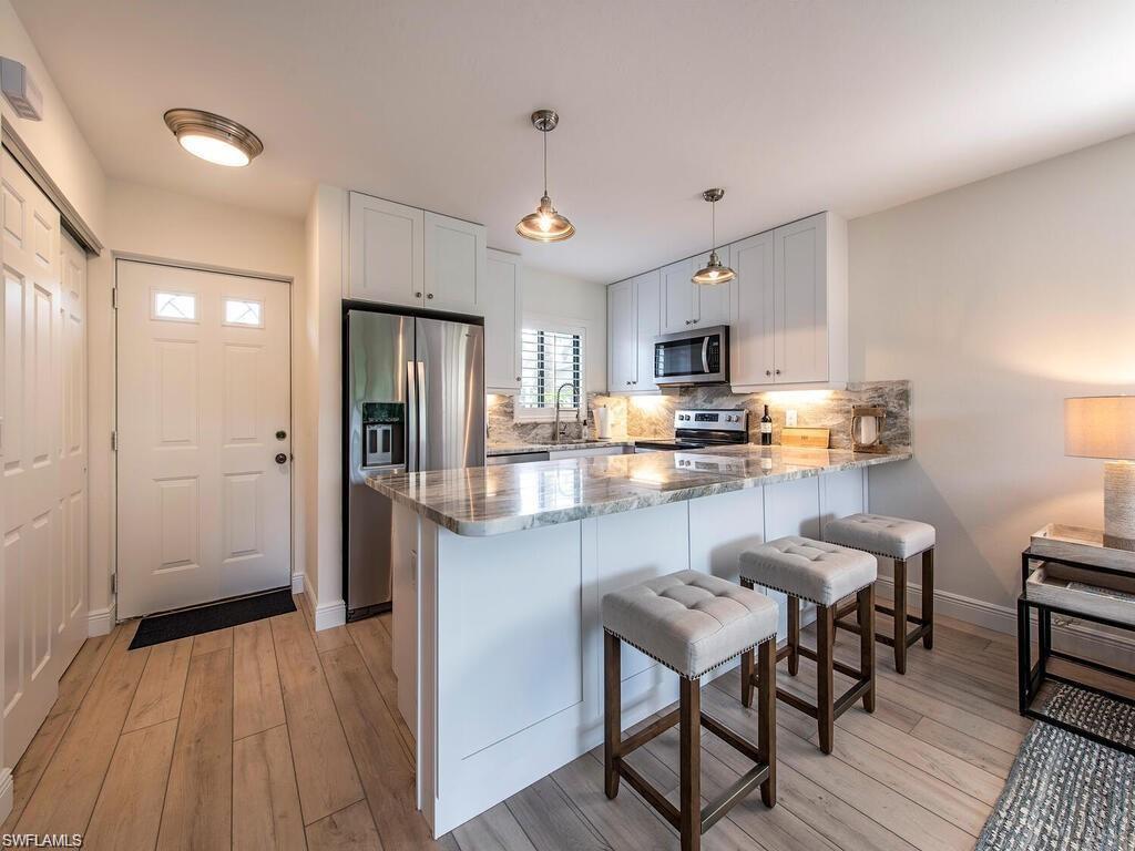 Image 2: Kitchen with a breakfast bar area, stainless steel appliances, a peninsula, decorative light fixtures, and light stone countertops