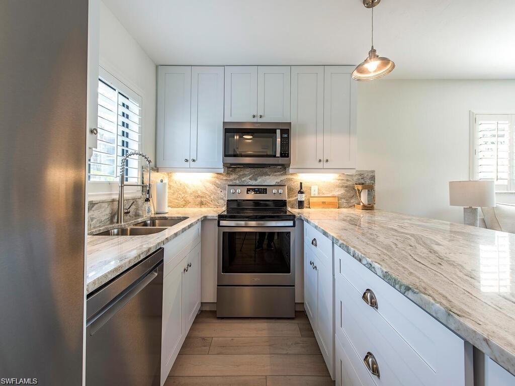 Image 4: Kitchen with stainless steel appliances, light stone countertops, decorative light fixtures, decorative backsplash, and light wood-style floors