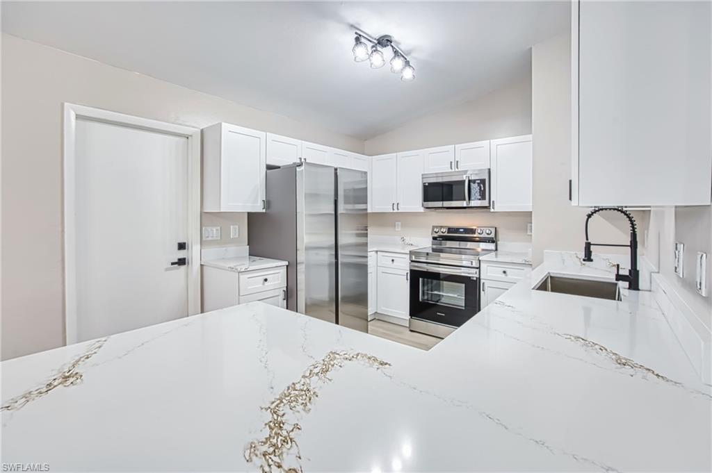 Image 4: Kitchen featuring appliances with stainless steel finishes, light stone countertops, lofted ceiling, and white cabinets
