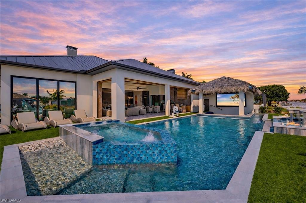 Image 1: Pool at dusk featuring a pool with connected hot tub, an outdoor hangout area, a patio area, and a yard