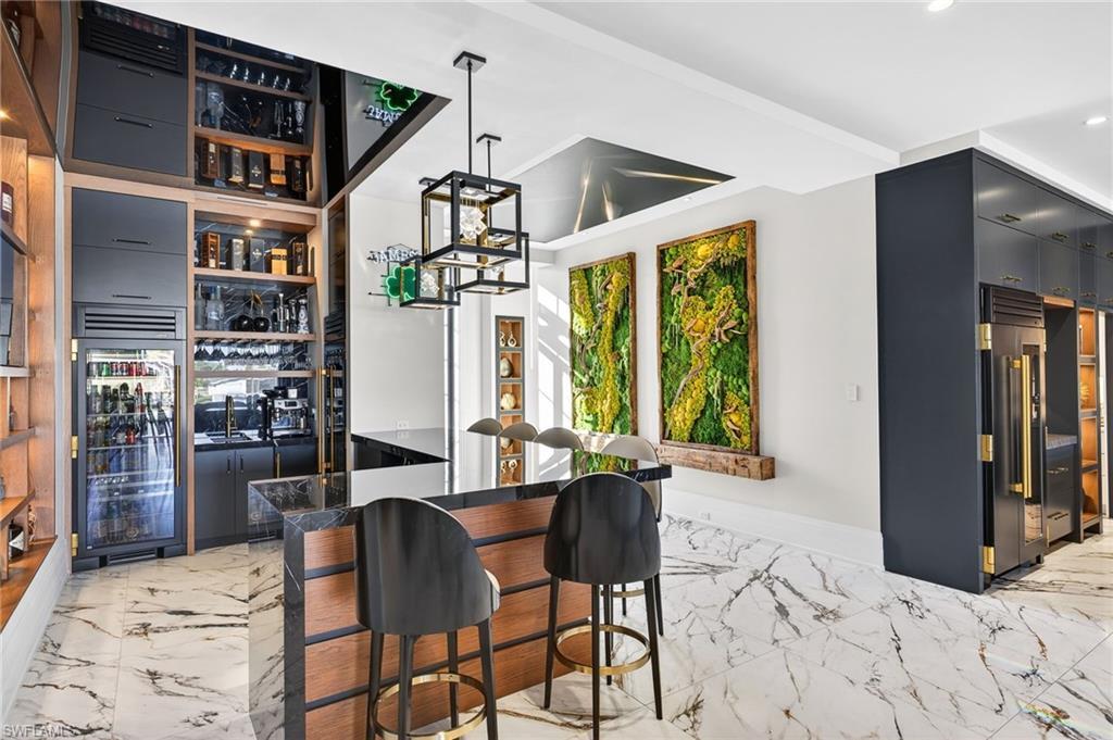 Image 4: Indoor wet bar featuring pendant lighting, high end refrigerator, dark cabinets, and modern cabinets
