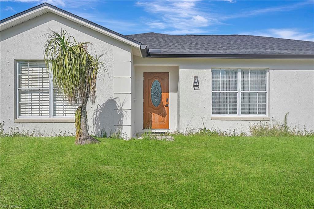 Image 2: Entrance to property with a lawn, stucco siding, and roof with shingles