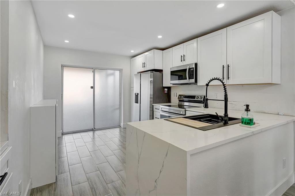 Image 3: Kitchen with stainless steel appliances, white cabinetry, wood tiled floors, light stone countertops, and recessed lighting