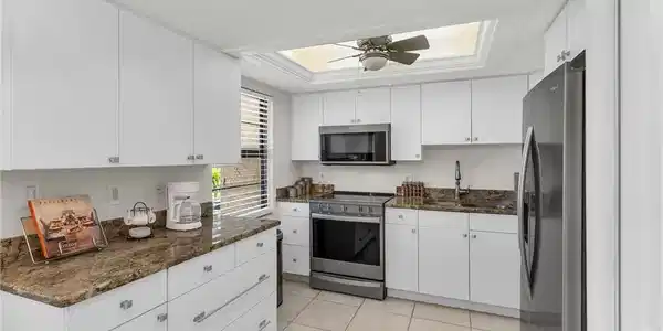 Image 3: Kitchen with appliances with stainless steel finishes, dark stone countertops, white cabinets, and a tray ceiling