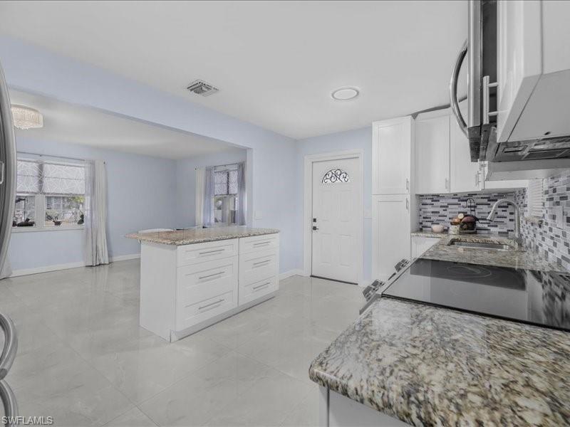 Image 2: Kitchen featuring white cabinetry, healthy amount of natural light, light stone counters, and decorative backsplash