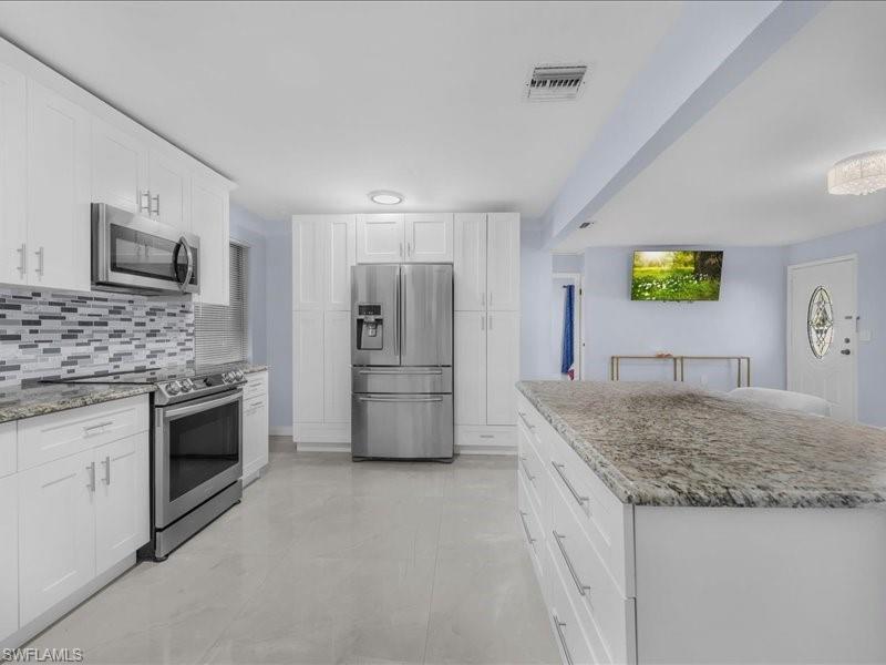 Image 3: Kitchen featuring stainless steel appliances, white cabinets, light stone counters, and tasteful backsplash