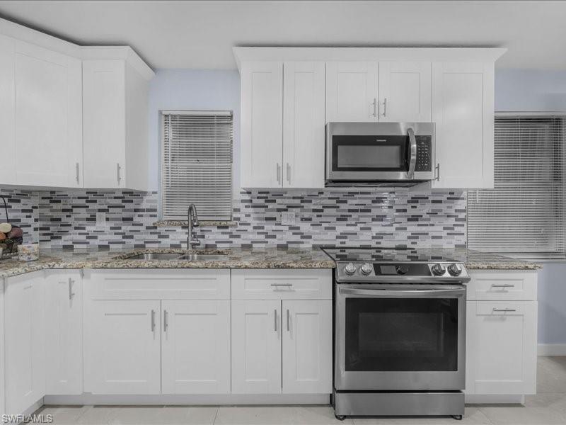 Image 4: Kitchen featuring stainless steel appliances, white cabinets, light stone counters, light tile patterned flooring, and backsplash