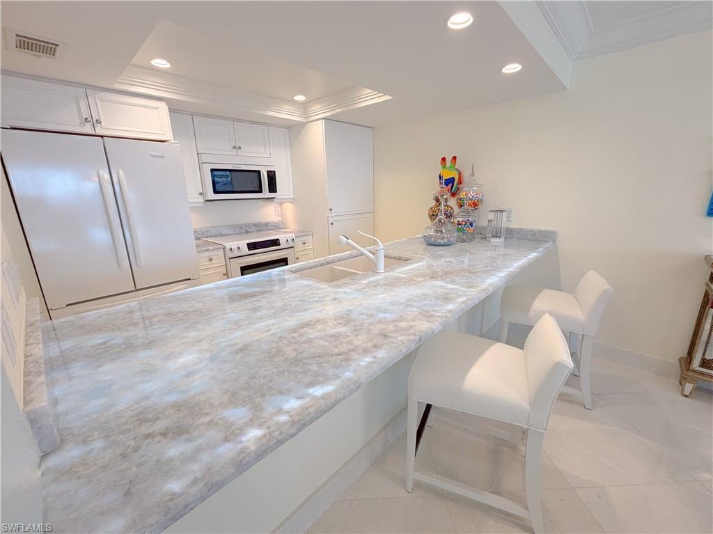Image 4: Kitchen featuring white appliances, sink, light stone countertops, white cabinetry, and a breakfast bar area