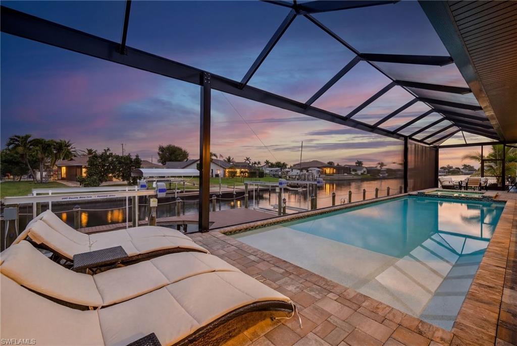 Image 3: Pool at dusk with boat lift, a water view, a sunroom, a boat dock, and a pool with connected hot tub