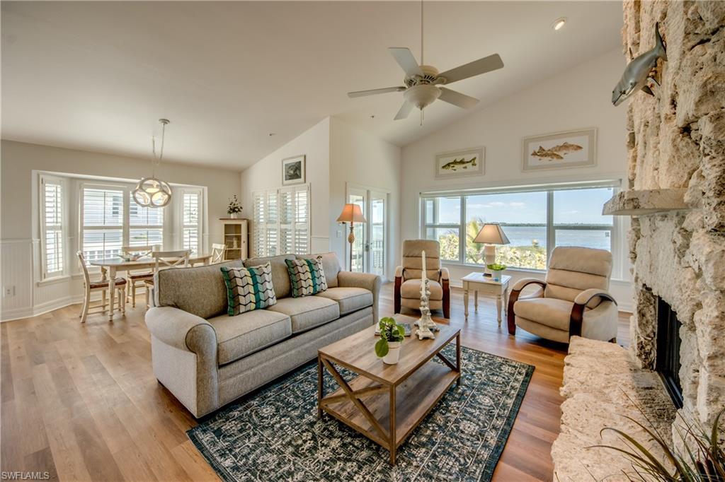 Image 3: Living area featuring vaulted ceiling, a fireplace, a ceiling fan, wood finished floors, and a water view