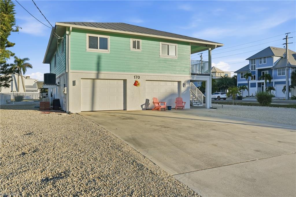 Image 4: Rear view of house featuring driveway, a balcony, an attached garage, a metal roof, and stairs - Virtually Edited Image