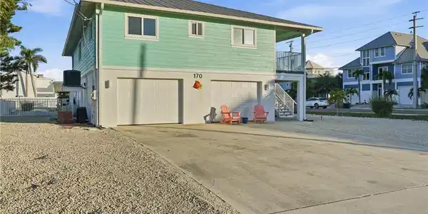Image 4: Rear view of house featuring driveway, a balcony, an attached garage, a metal roof, and stairs - Virtually Edited Image