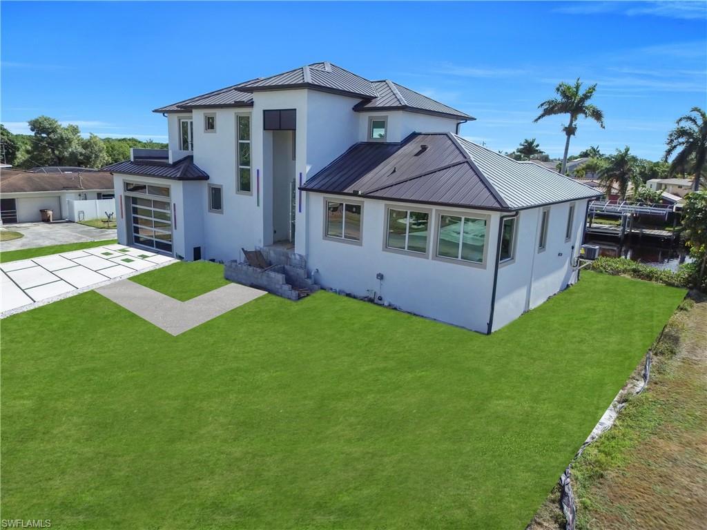 Image 2: Rear view of property featuring a standing seam roof, concrete driveway, stucco siding, and a garage