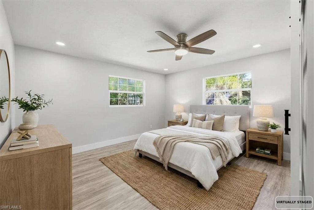 Image 3: Bedroom 1 with light wood-style floors, a ceiling fan, multiple windows, and recessed lighting- virtually stage
