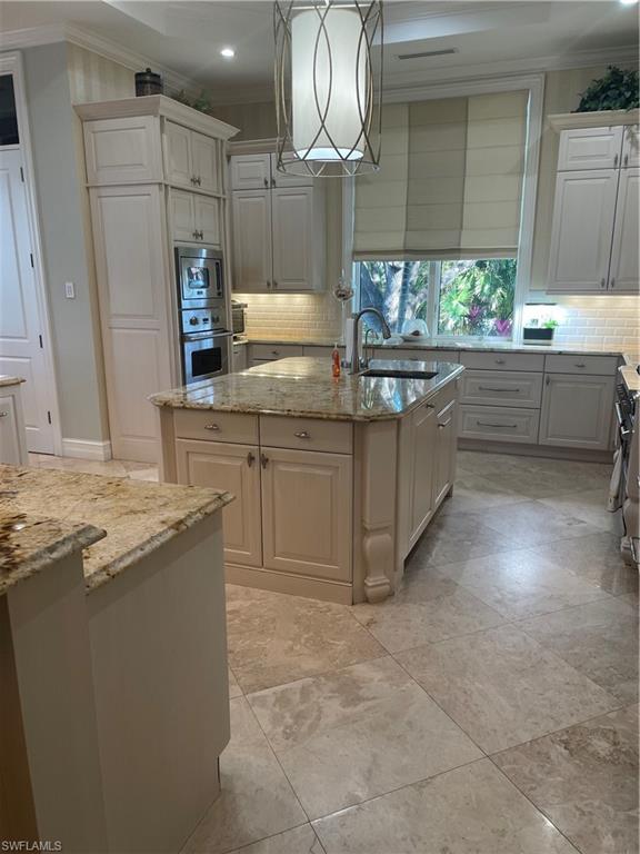 Image 3: Kitchen with pendant lighting, an island with sink, sink, oven, and light stone countertops